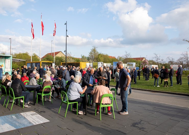Borgere sidder og står i området mellem Brønden og Strandboxen, i baggrunden ses udstillingen af forslagene til udviklingsplanen. 